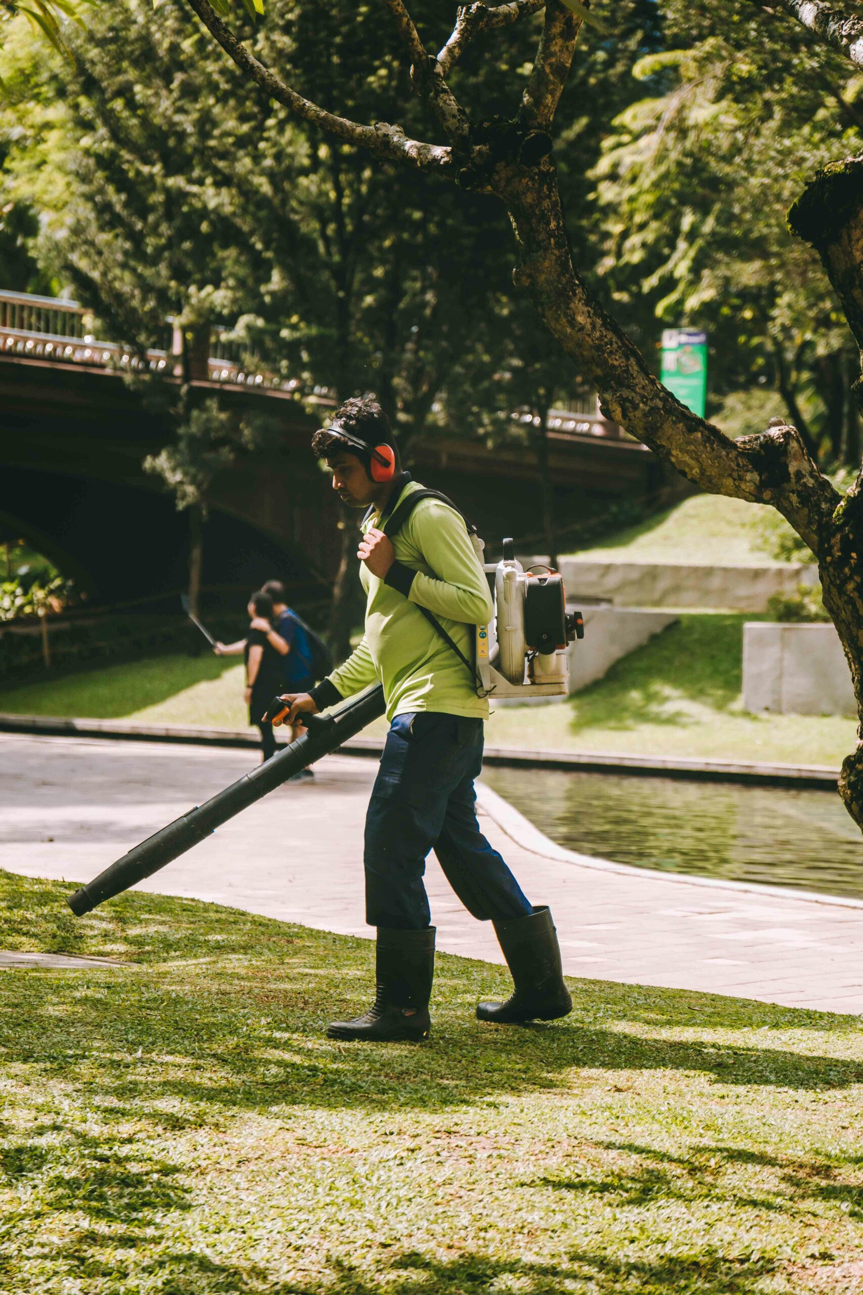 Gardener operates a leaf blower in a sunlit park in Kuala Lumpur, Malaysia.